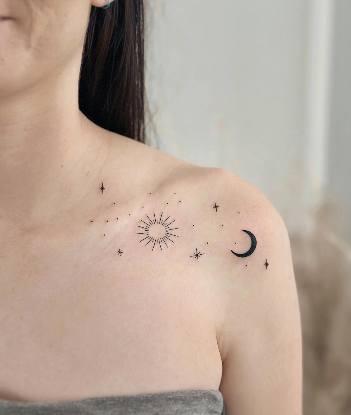 Fine line celestial tattoo of a sun, moon, and stars across the collarbone and shoulder