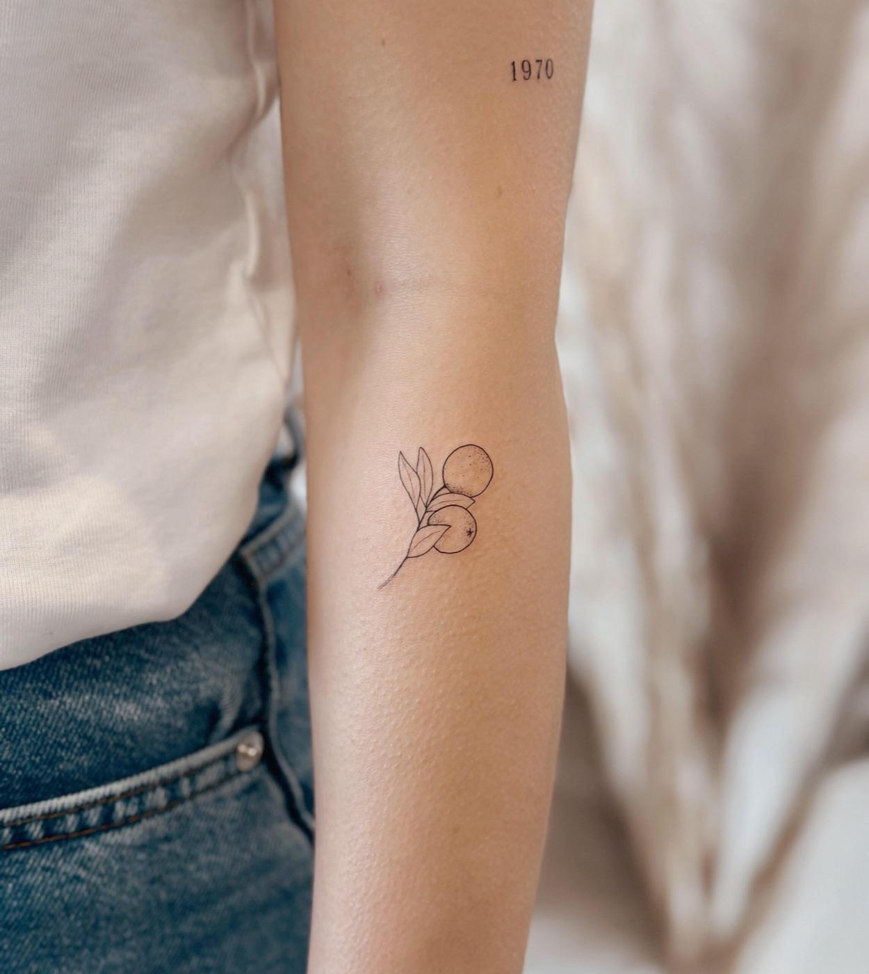 Fine line citrus branch tattoo with leaves and fruit on the upper arm