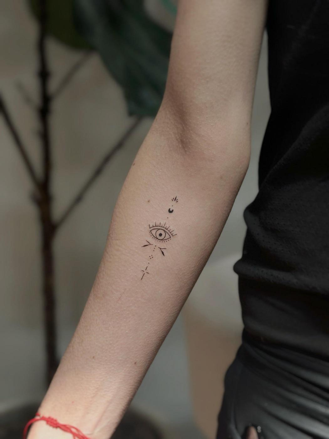 Small fine line evil eye tattoo with celestial details on the inner forearm
