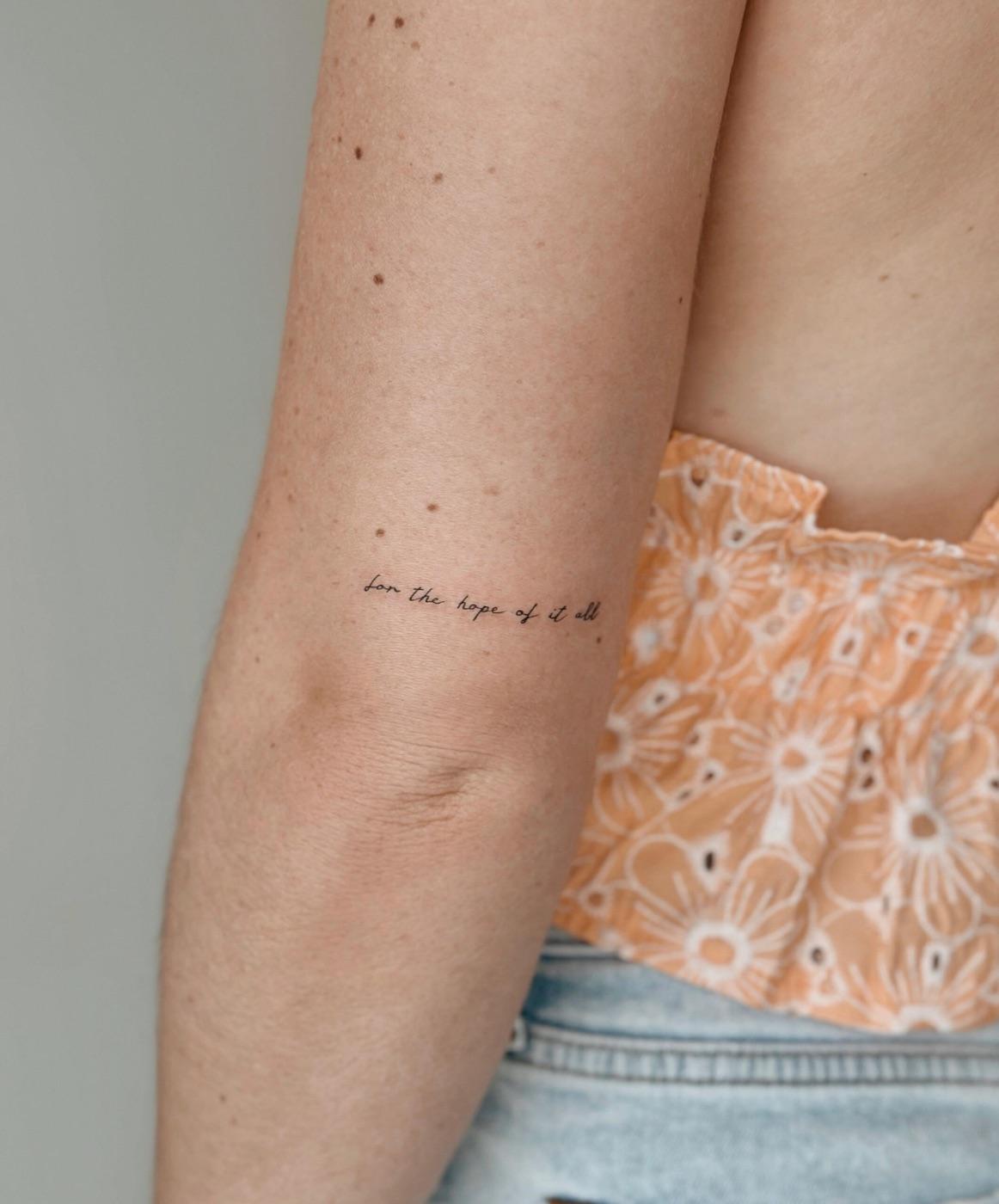 Delicate fine line script tattoo reading a short quote on the inner arm