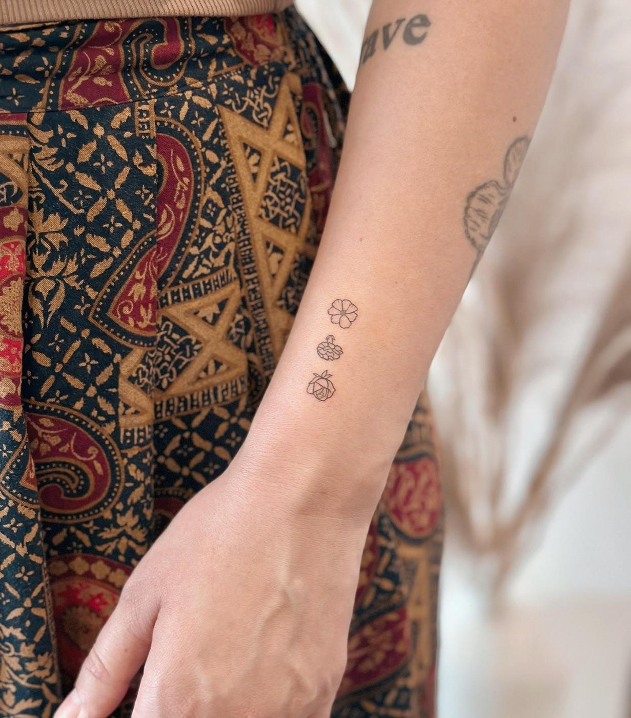 Three small fine line flowers stacked vertically on the inner forearm