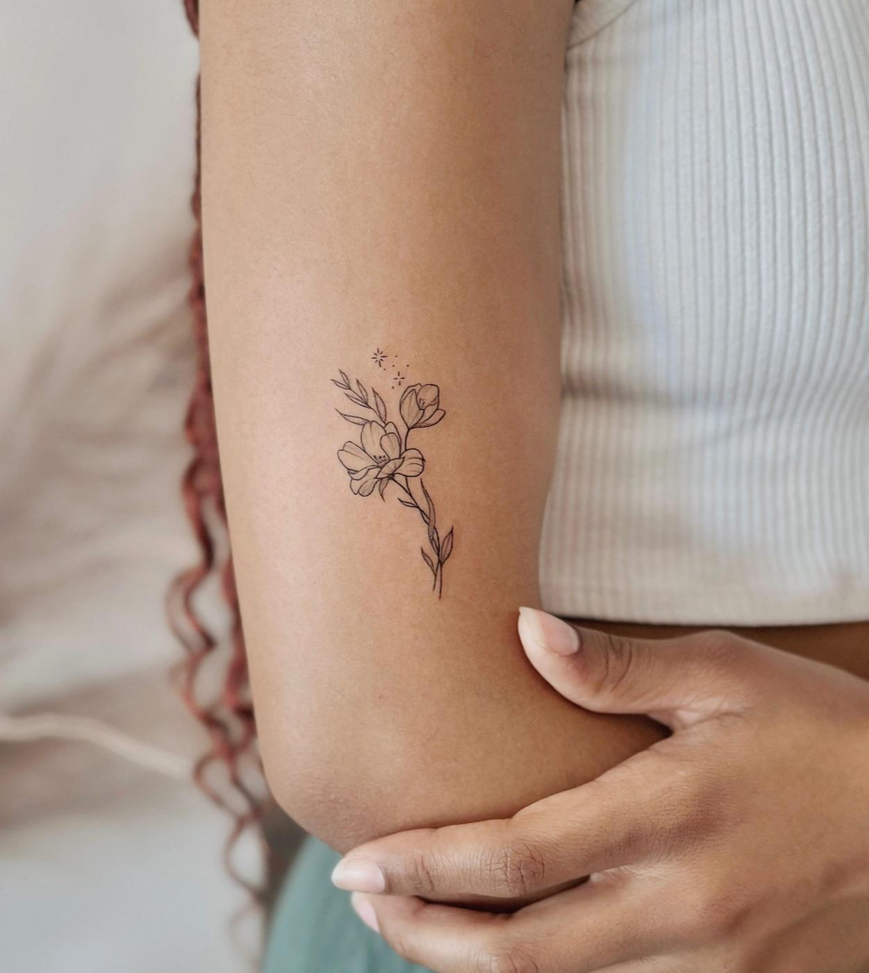 Fine line wildflower tattoo with delicate leaves and blossoms on the back of the arm near the elbow