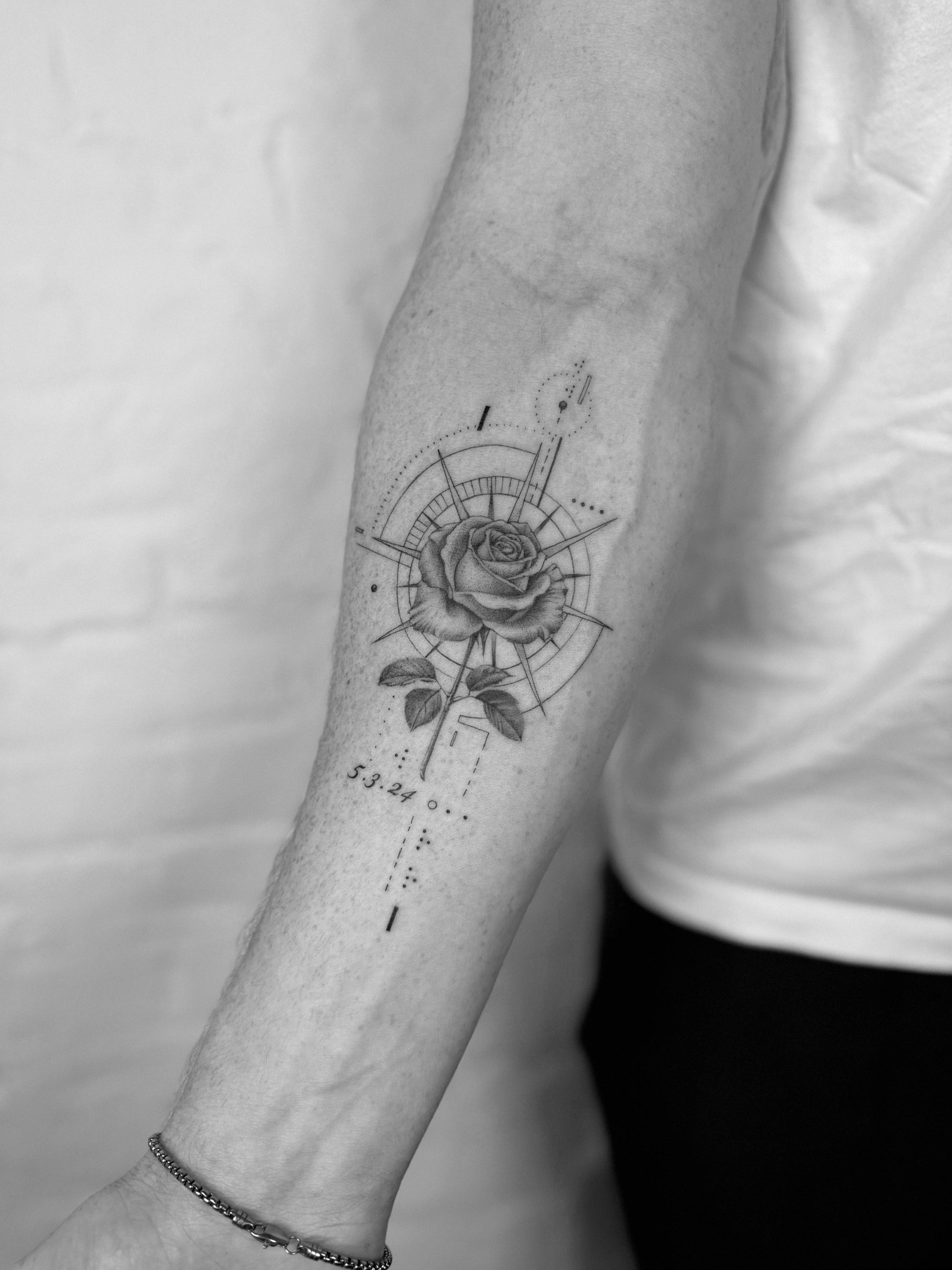 Black and grey rose tattoo with geometric compass linework on the forearm