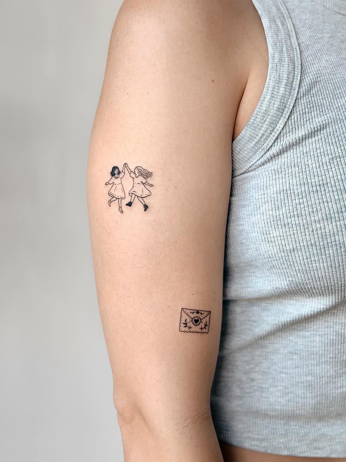 Fine line tattoo of two girls holding hands beside a small envelope