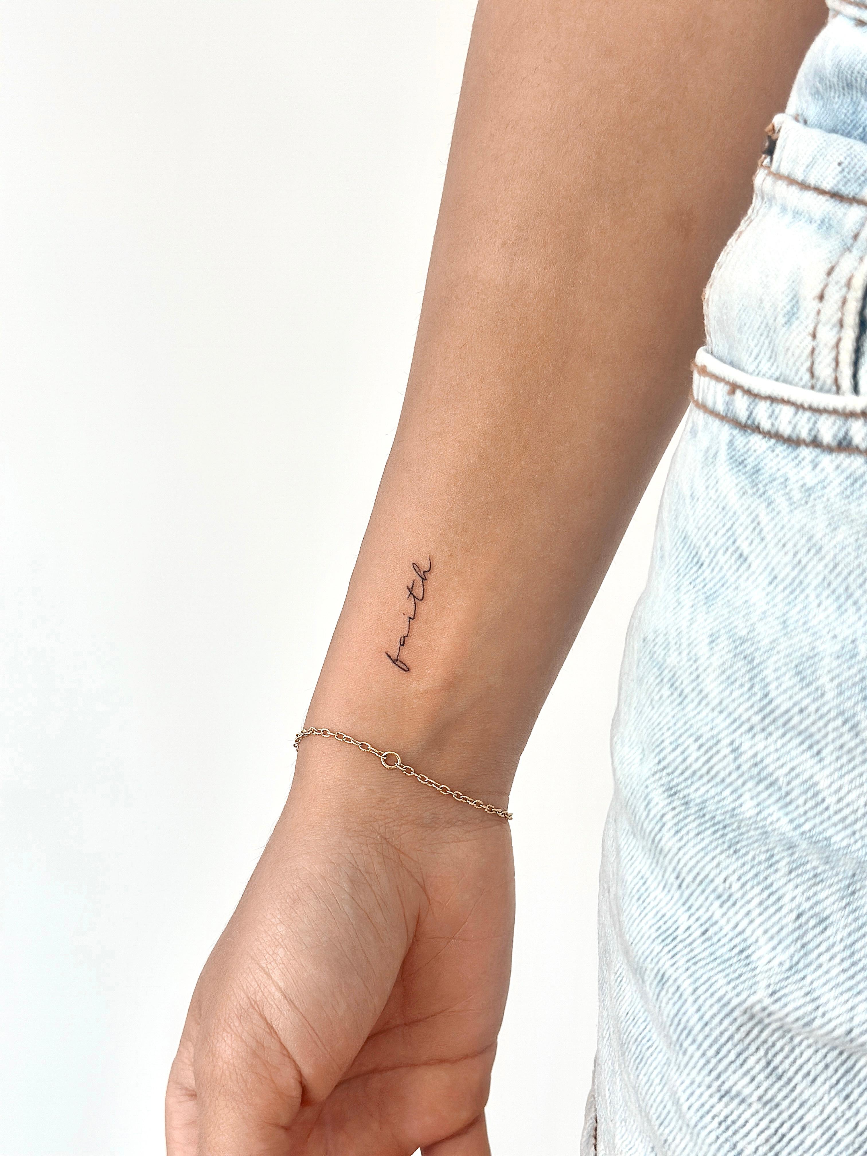 Fine line script tattoo reading faith on the wrist