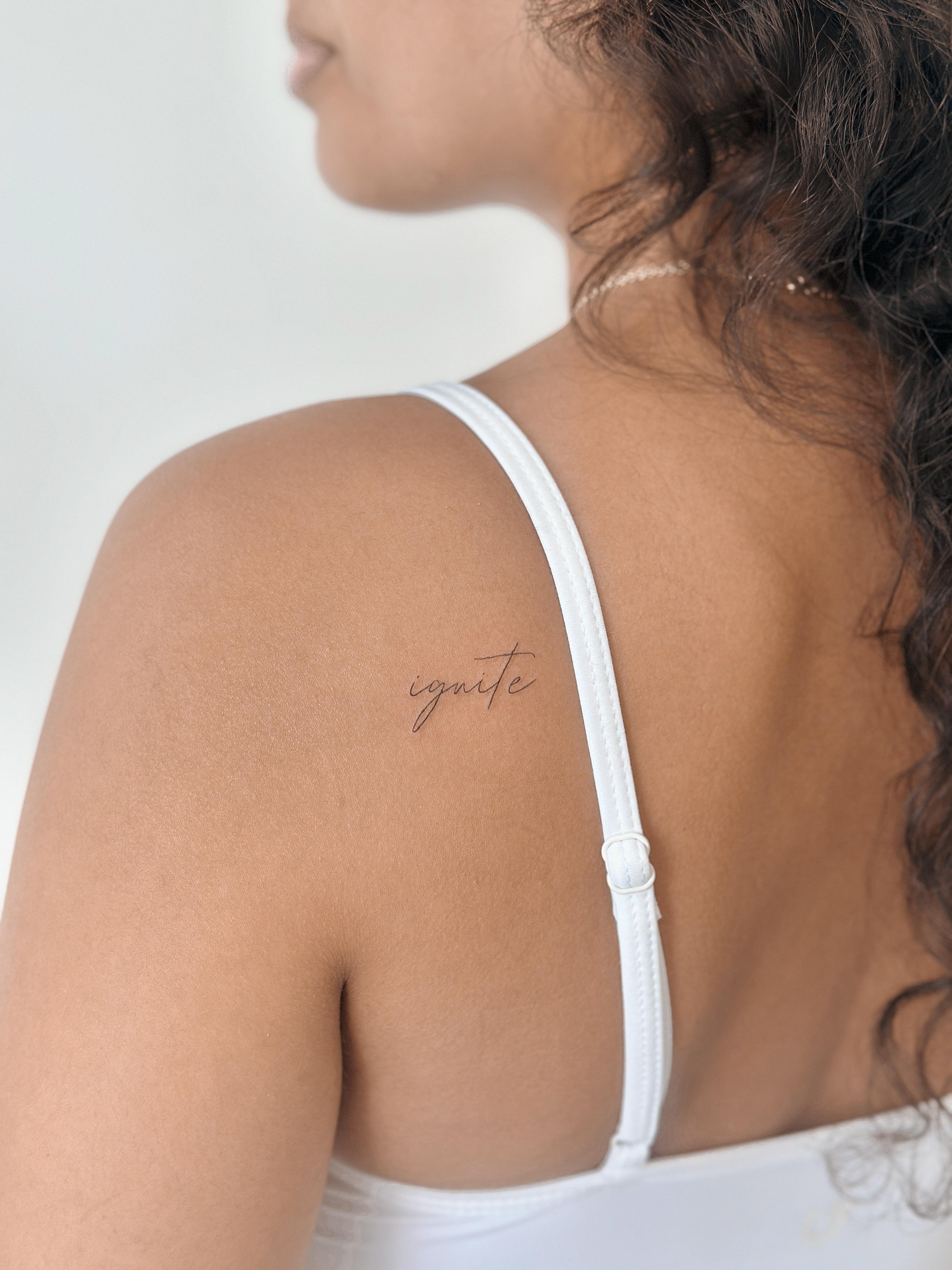 Fine line script tattoo reading ignite on the shoulder blade