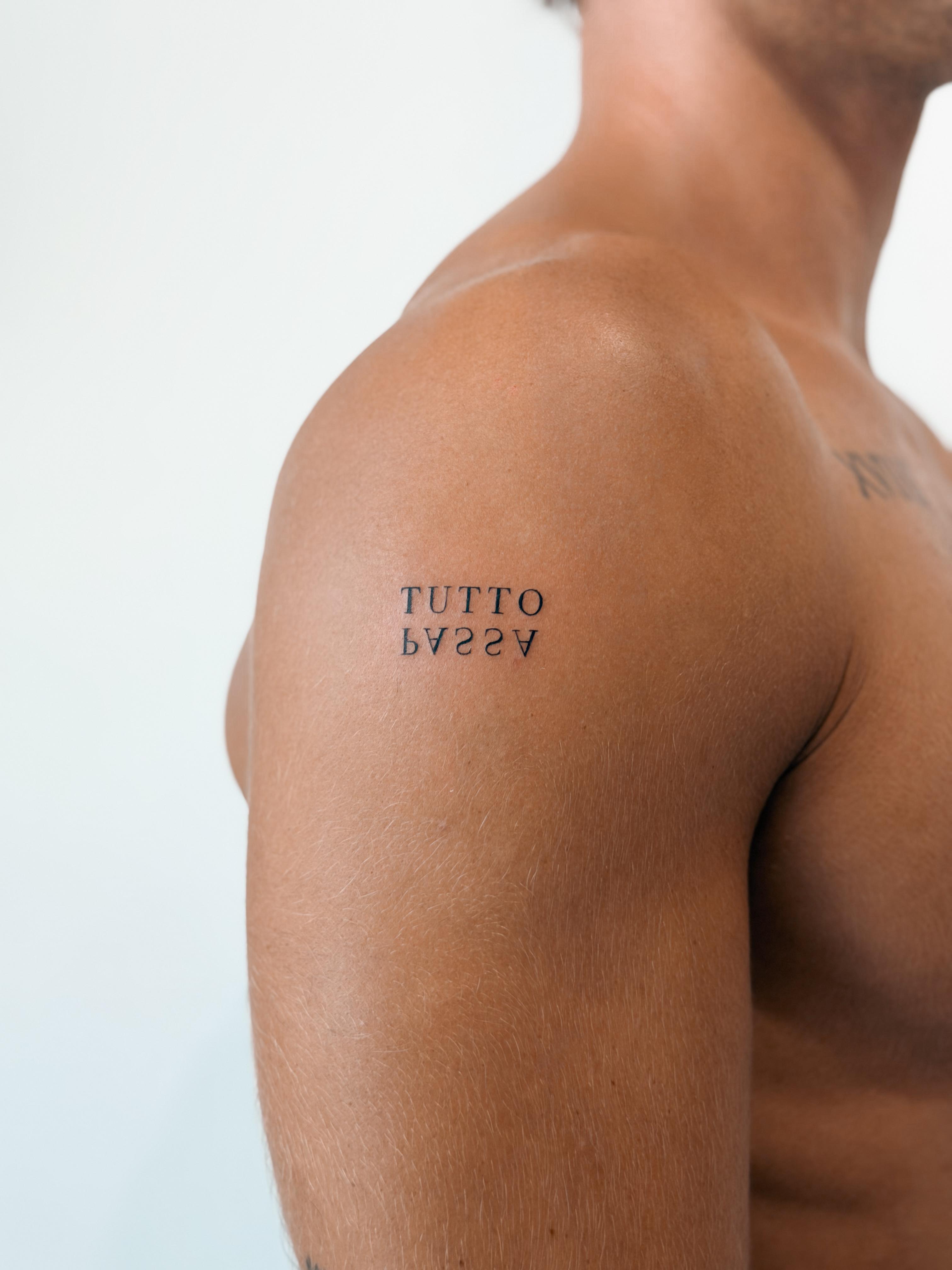 Serif lettering tattoo reading Tutto Passa on the shoulder