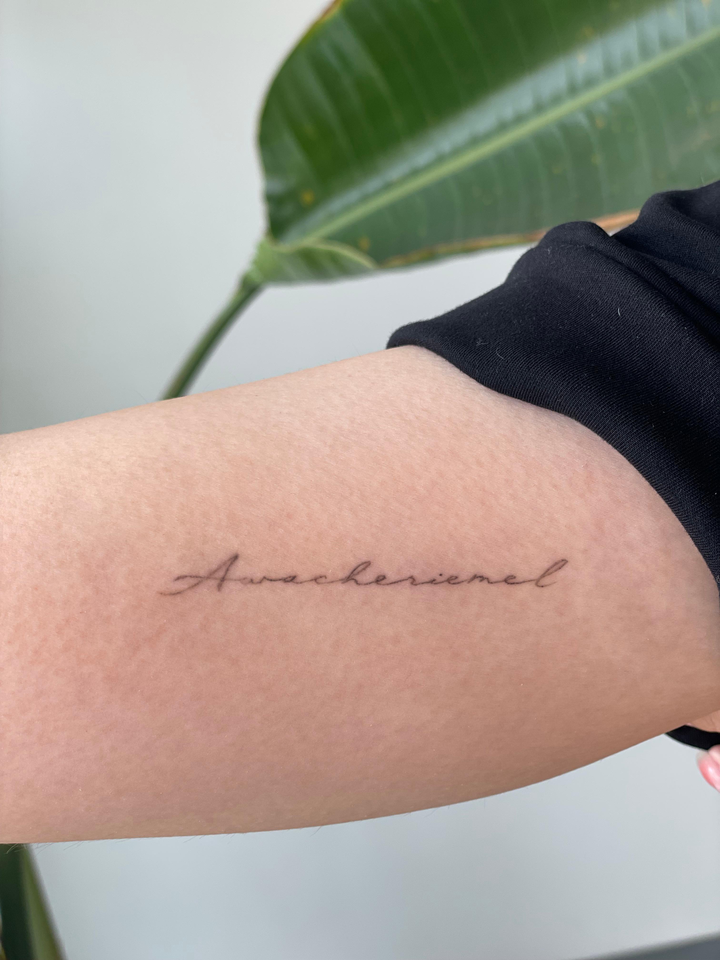 Fine line cursive script tattoo on the upper arm
